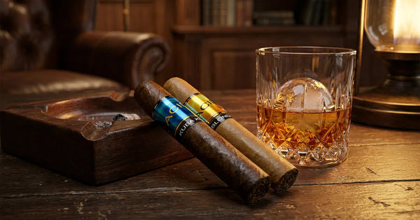 Acid Kuba Kuba and Blondie cigars by Drew Estate on a wooden table with a drink.