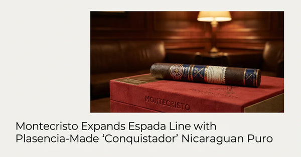 Montecristo Espada Conquistador cigar resting on its signature red suede and gold box in a luxury lounge setting.